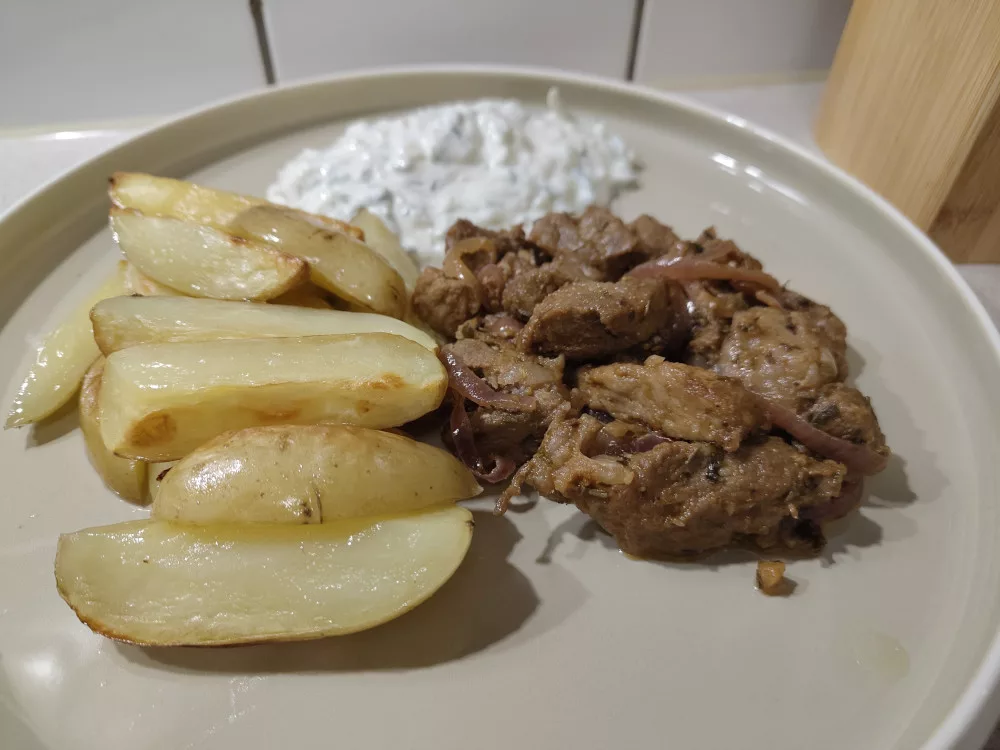 Eine Portion des gebratenen Fleisches mit Kartoffelwedges und Tsatsiki auf einem Teller