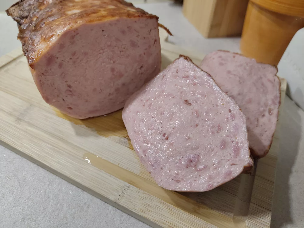 Ein angeschnittener Leberkäse auf einem Holzbrett.