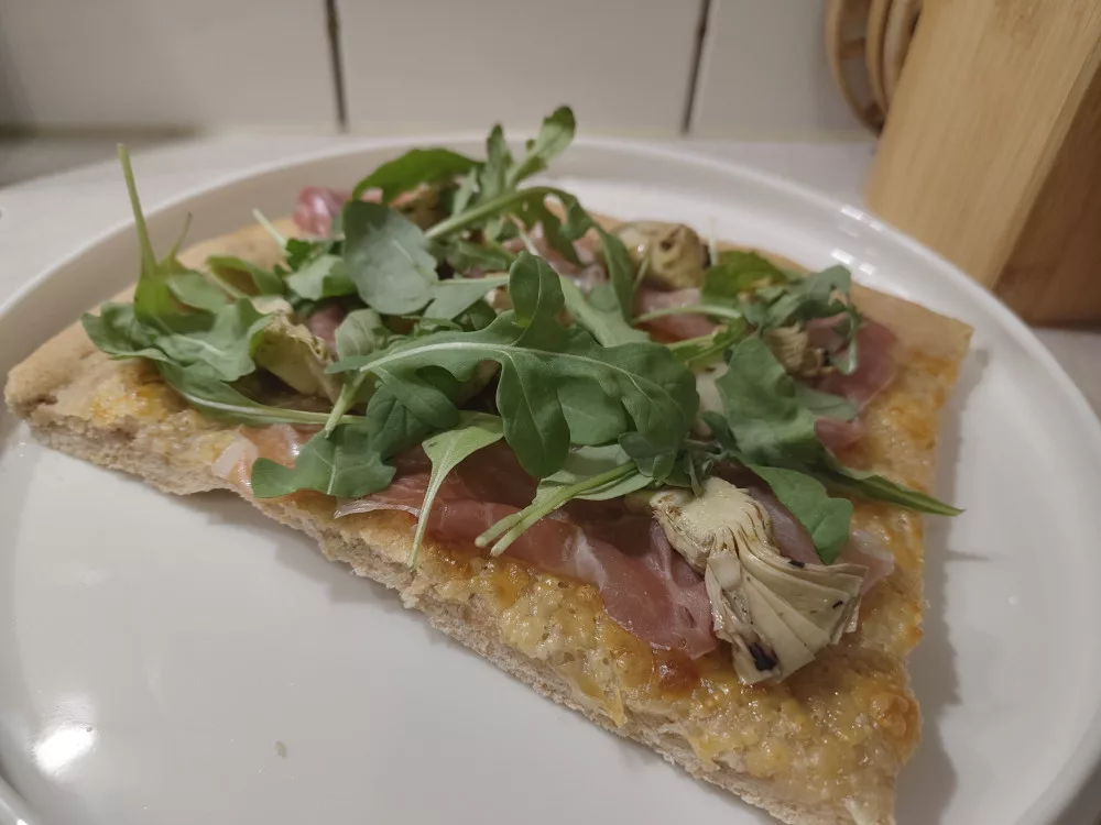 Ein Stück der Pizza Bianca belegt mit Prosciutto, Artischockenherzen und Rucola