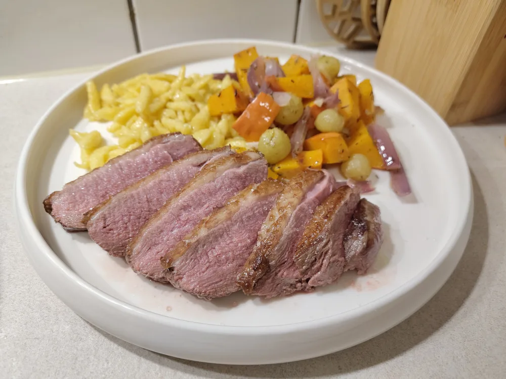 Spätzle neben Kürbis-Trauben Gemüse neben einigen Scheiben gebratene Entenbrustfilet