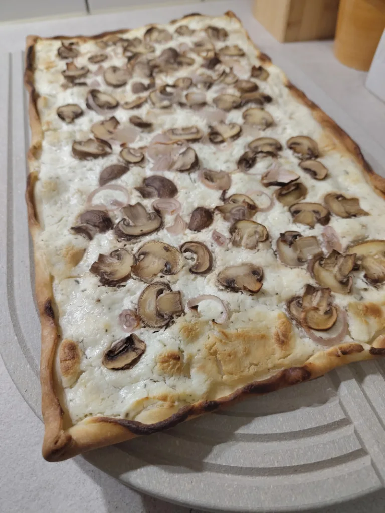 Der fertige Flammkuchen liegt nach dem Backen auf einem großen Schneidebrett.