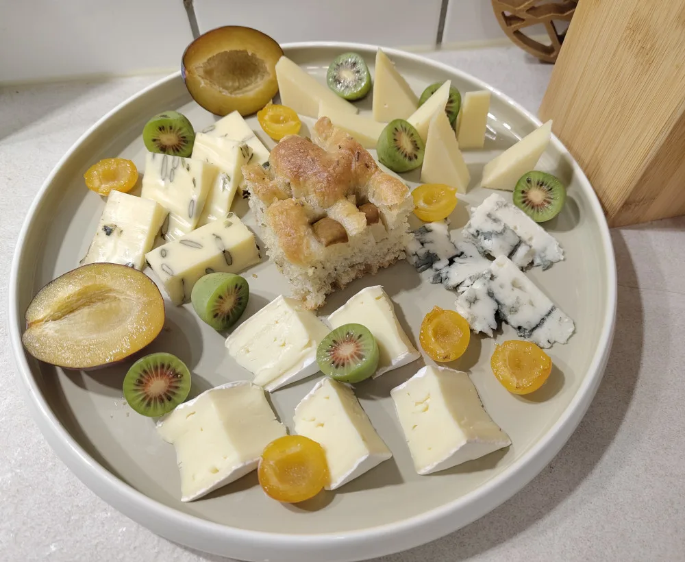 Ein großer Teller gefüllt mit geschieden geschnittenen Käse, Zwetschgen, Mirabellen, Kiwibeeren und ein exemplarisches Stück einer Focaccia
