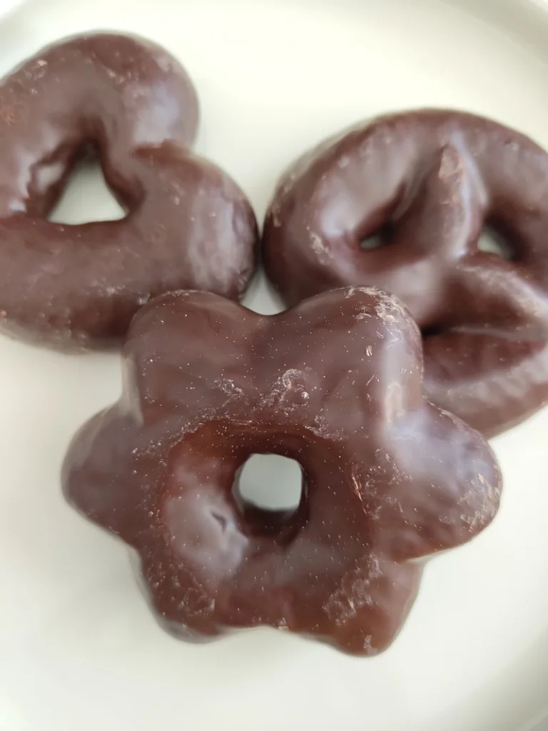 Drei Lebkuchen mit Zartbitter-Schokoladenüberzug in verschiedenen Formen (Herz, Stern, Brezel) auf einem weißen Teller.