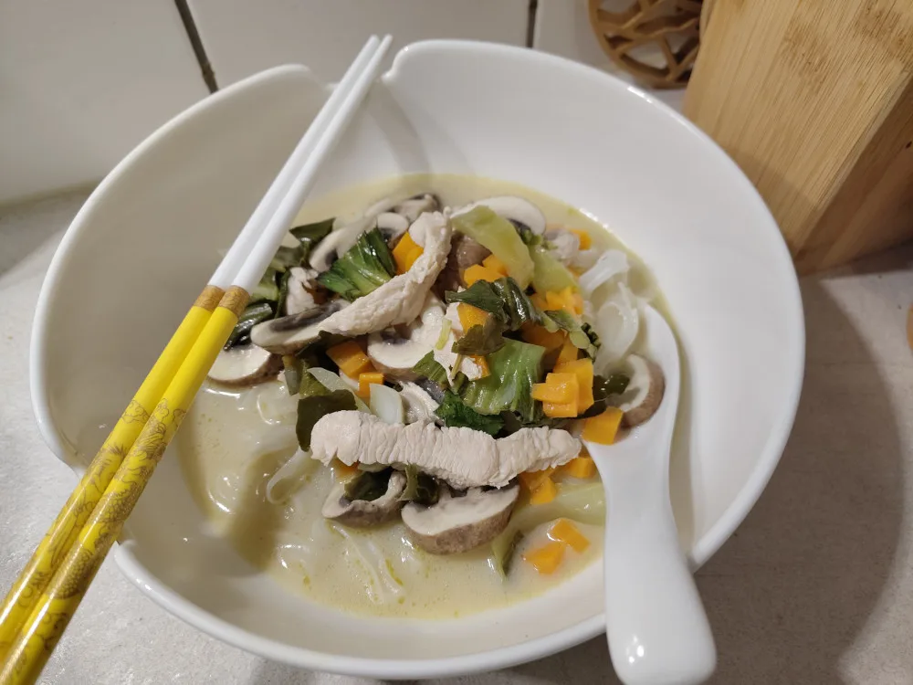 Eine Schüssel gefüllt mit Reisnudeln und der Tom Kah Gai Suppe.