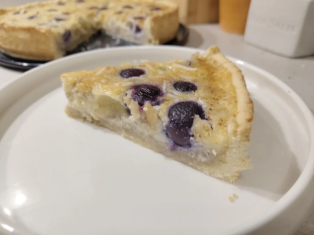Im Vordergrund ein Stück der Traubenwähe auf einem Teller, dahinter der angeschnittene Kuchen. Es wurden grüne und rote Trauben für den Kuchen verwendet.