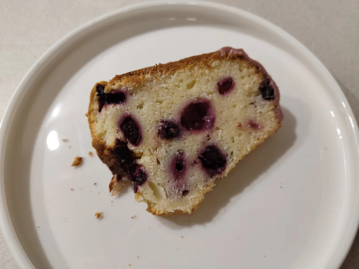 Ein Stück des Gugelhupfes auf einem weißen Teller. Man sieht die vielen Beeren im lockeren hellen Quarkteig.