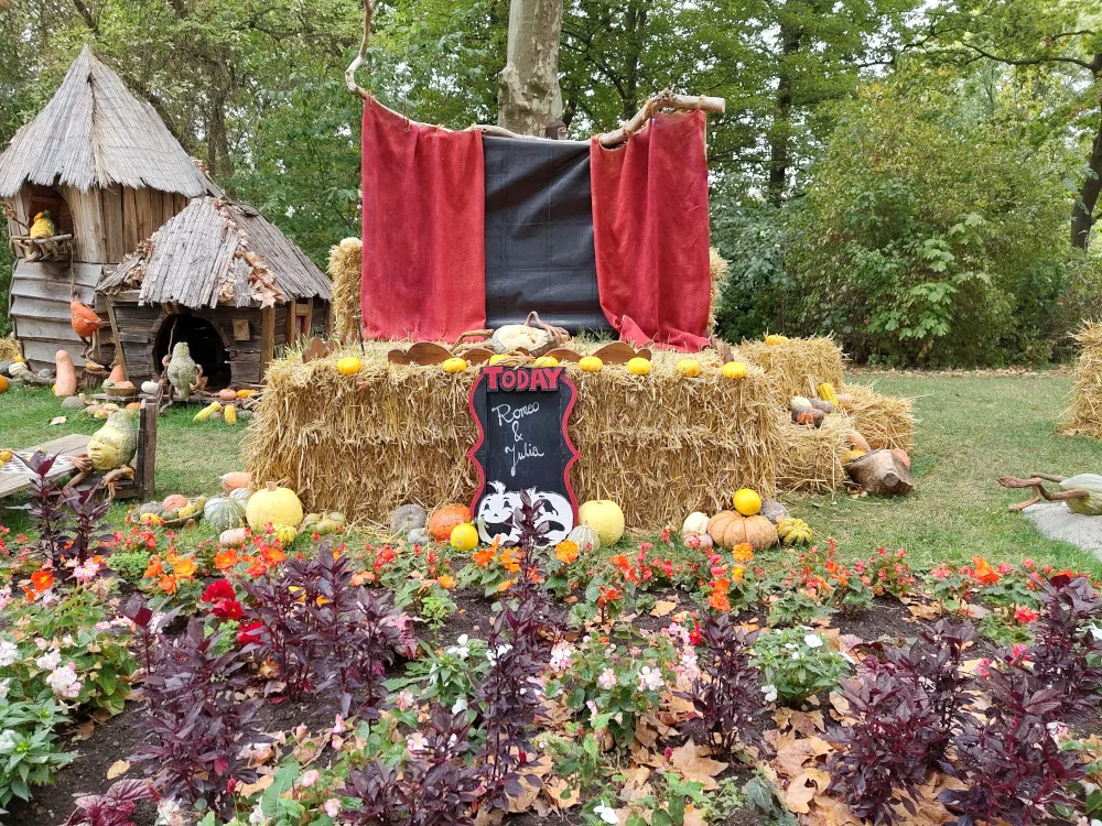 Eine Bühne aus Strohballen mit einem Theatervorhang dahinter. Auf der Bühne liegt ein ermordeter Romeo in Gestalt eines Kürbis-Gnomes